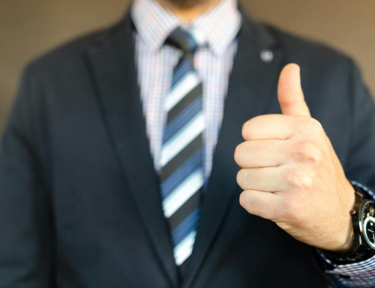 Close-up of a businessman in a suit giving a thumbs up gesture, symbolizing success.