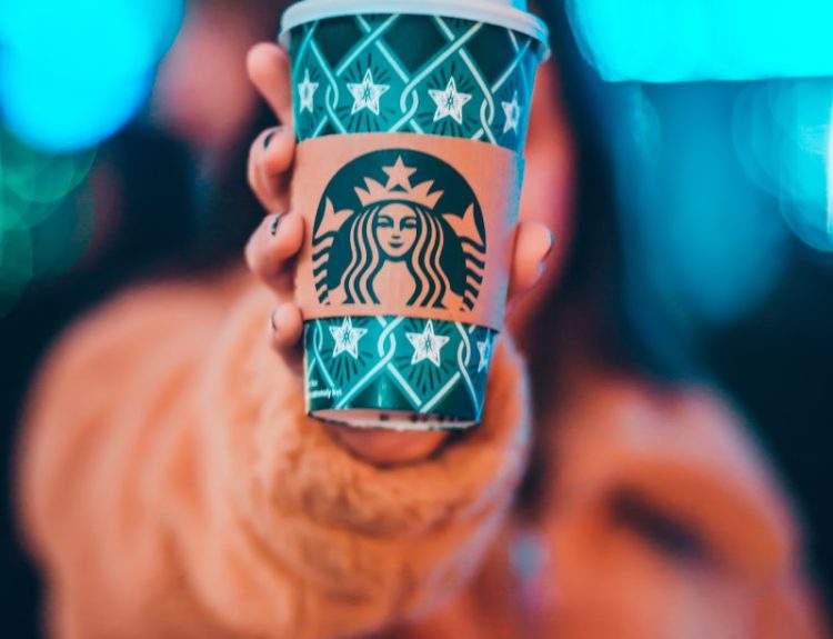 woman on brown jacket showing green and brown Starbucks coffee cup