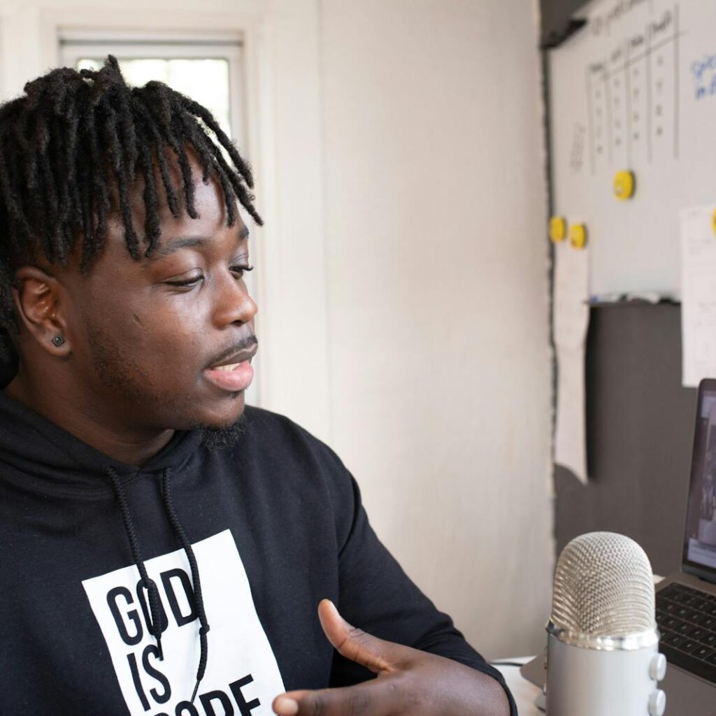 Man recording a podcast indoors with a laptop and microphone, focused and speaking.