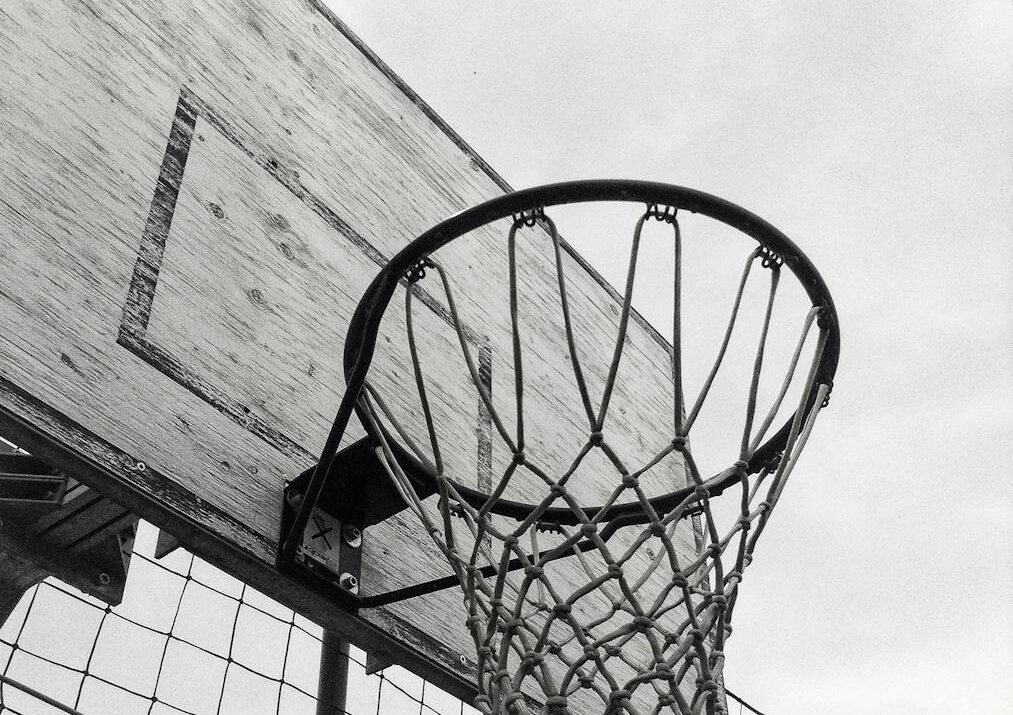 Monochrome shot of a basketball hoop against the sky, capturing the essence of outdoor sports.