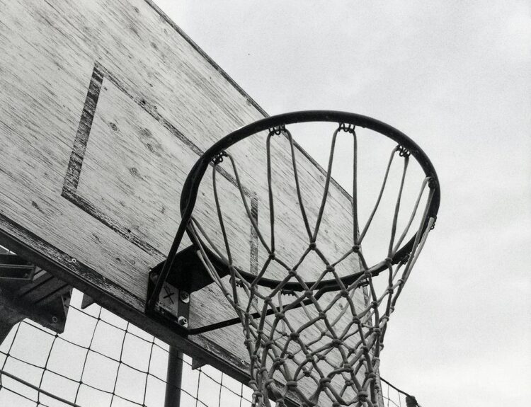 Monochrome shot of a basketball hoop against the sky, capturing the essence of outdoor sports.